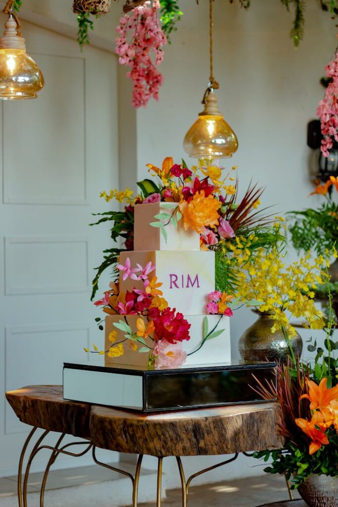 A three-tier wedding cake adorned with colorful flowers, set in a beautifully decorated space.