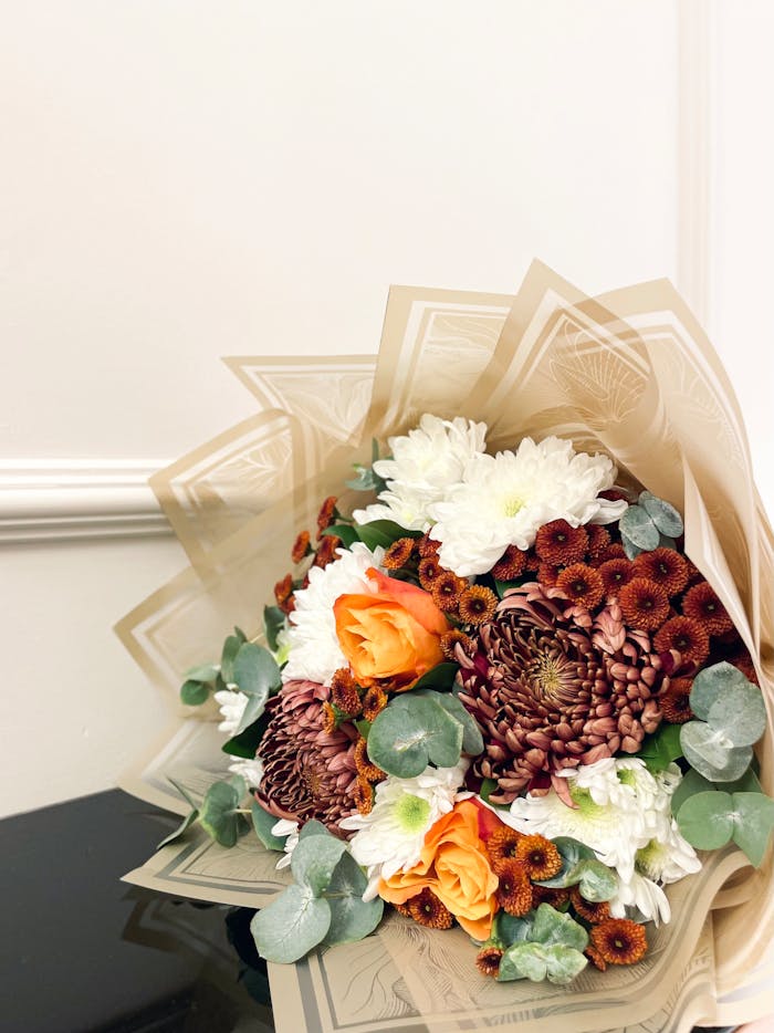 A vibrant bouquet with chrysanthemums, roses, and greenery in elegant wrapping.