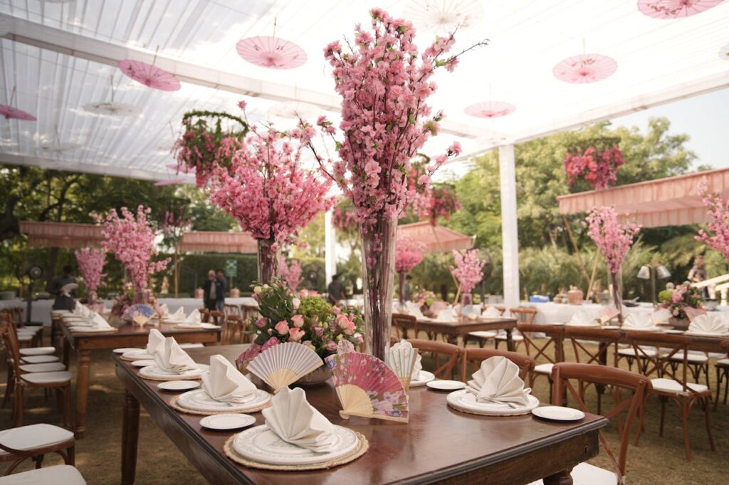 Stunning outdoor Indian wedding setup with pink floral decor and traditional fans.