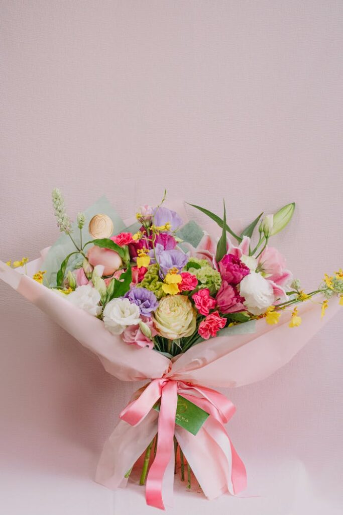 Beautifully arranged bouquet of mixed flowers with a pink ribbon against a soft pastel background.